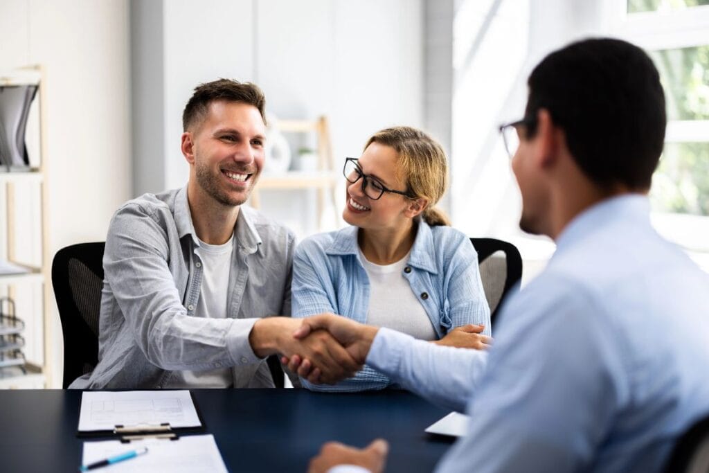 Couple meeting with a social worker or advisor in a bright, modern office setting, smiling and shaking hands during a consultation.